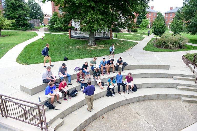 Aerial shot of students sitting on steps listening to professor lead class discussion