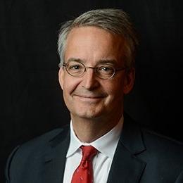 Person wearing dark suit jacket and red tie smiling 