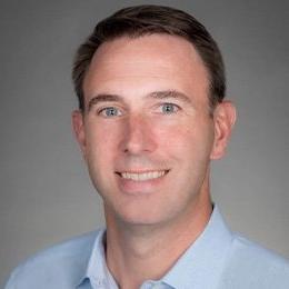 Person wearing light blue shirt in front of grey background smiling